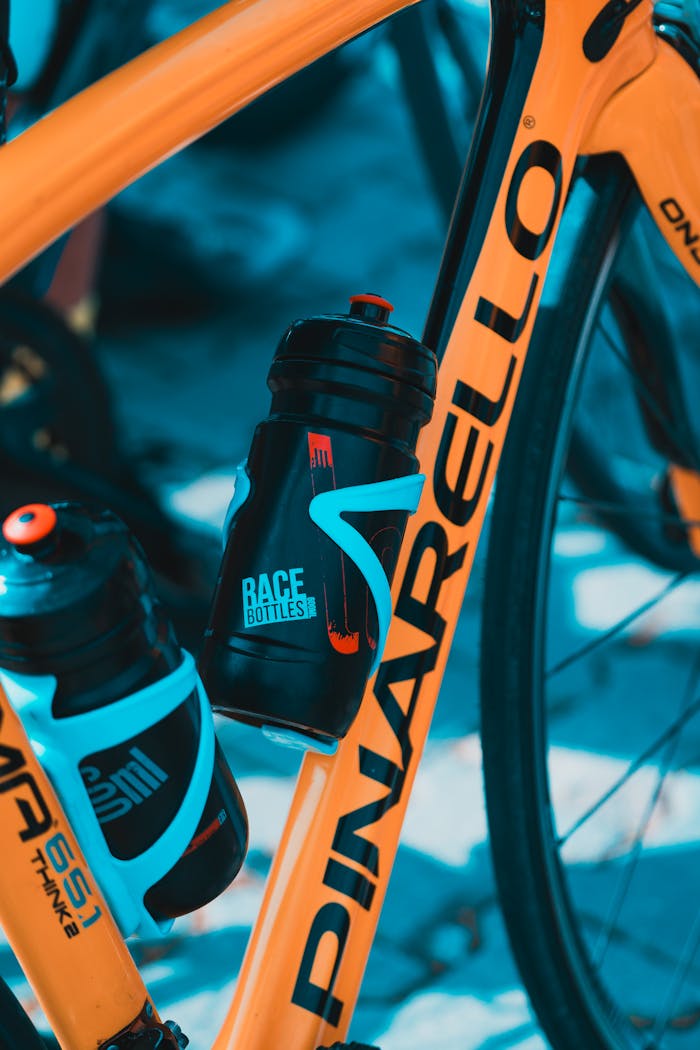 Orange bicycle with mounted water bottles, ideal for cycling or sports imagery.