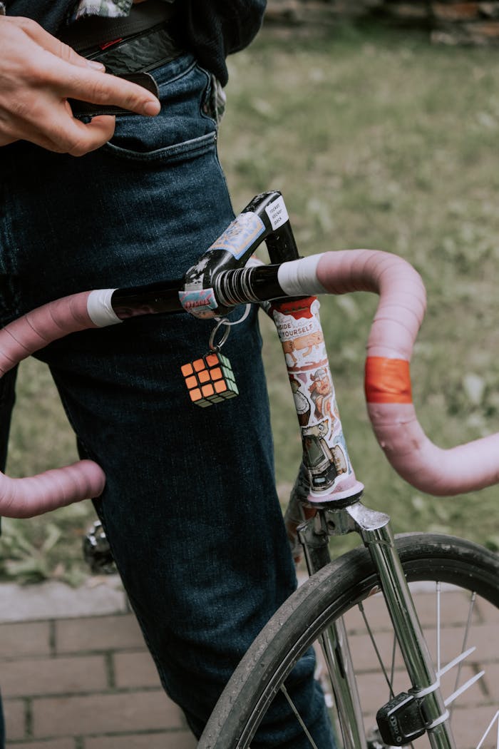 services-img Close-up of a bicycle with a Rubik's cube hanging from the handlebar, featuring pink grips and denim pants.