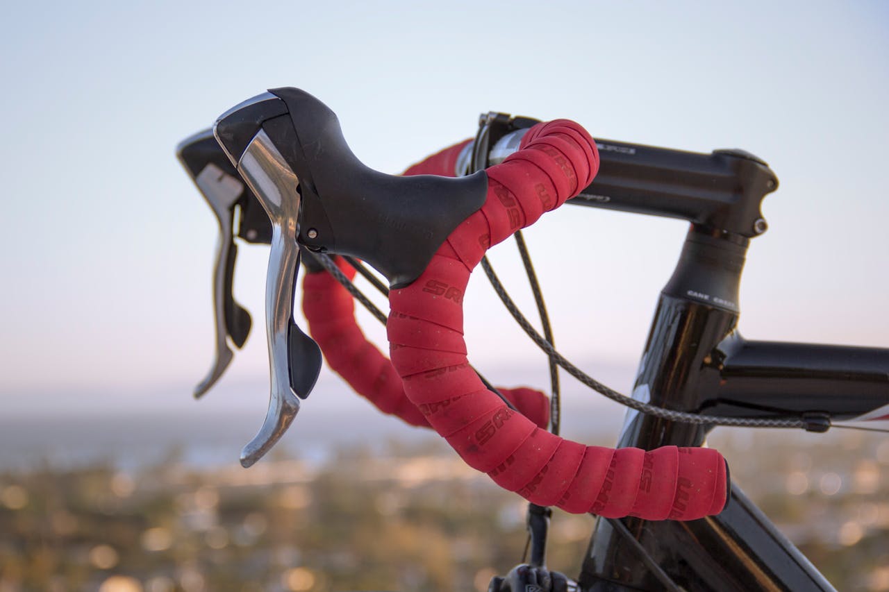 Detailed view of red handlebars on a racing bicycle with blurred background at sunset.